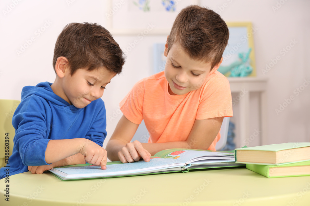 Cute little boys with book sitting at table, closeup Cute little boys with book sitting at table, closeup