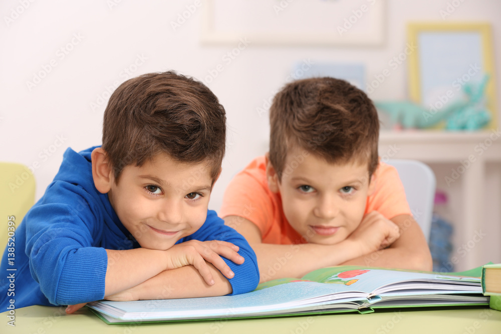 Cute little boys with book sitting at table, closeup Cute little boys with book sitting at table, closeup