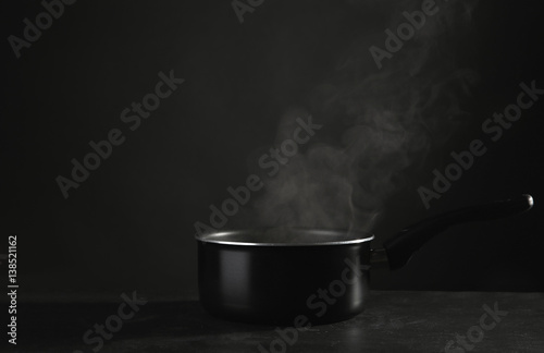 Saucepan with hot liquid on table against dark background