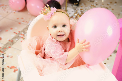 Cute little birthday girl playing with balloon while sitting on high chair