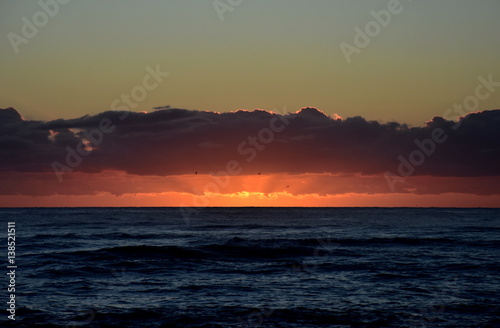 Beautiful sunrise cloudscape over ocean background. Sun rays beaming through picturesque clouds above sea. Blue sky with clouds  sea and sun on the horizon. Beautiful sunrise over the quiet calm sea.