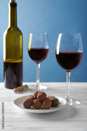 Chocolate truffles and glasses with red wine on white wooden table
