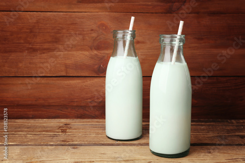 Two bottles of milk with straws on wooden background