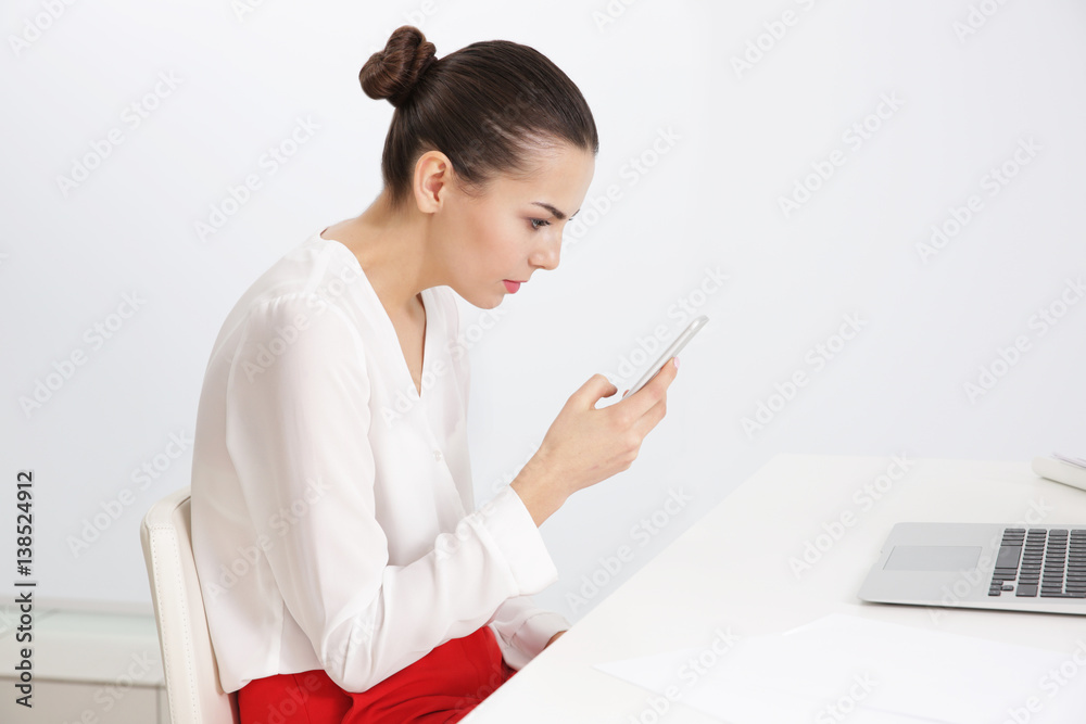Incorrect posture concept. Young woman with phone sitting at table indoors - obrazy, fototapety, plakaty 