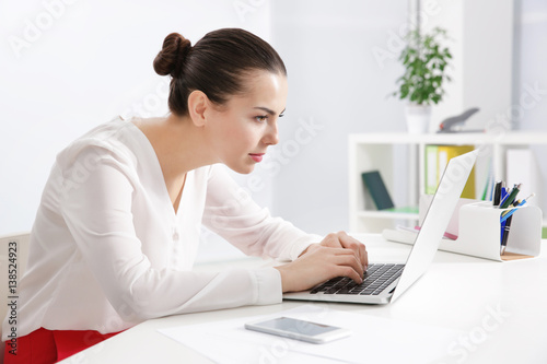 Incorrect posture concept. Young woman sitting at table in modern room photo