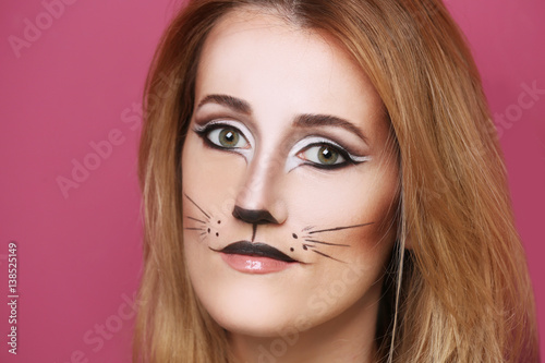 Beautiful young woman with cat makeup on color background