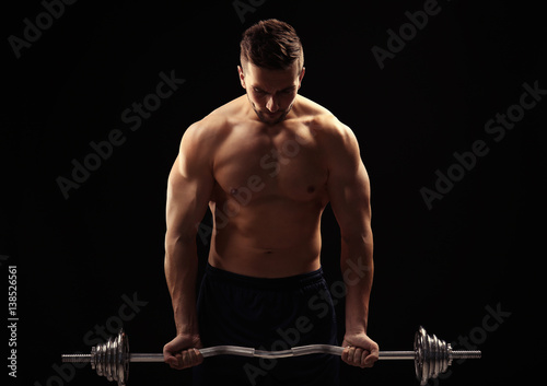 Sporty man doing exercises with barbell on black background