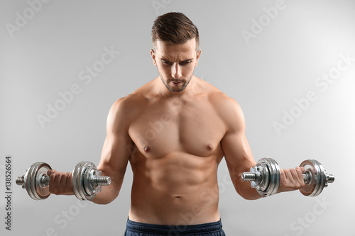 Sporty man doing exercises with dumbbells on light background