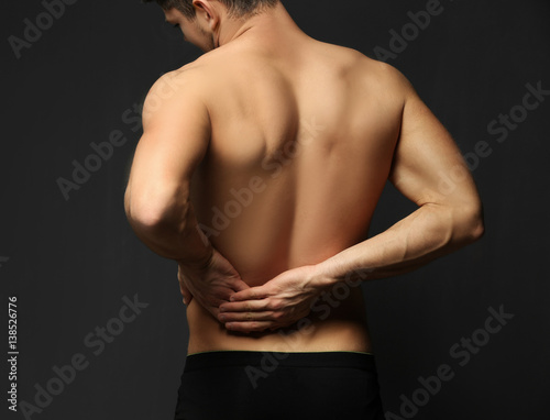 Young man suffering from backache on dark background