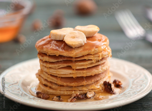 Tasty pancakes with banana, nuts and honey on plate