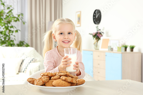 Cute girl with glass of milk and cookies at home