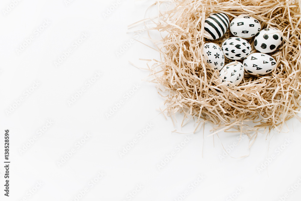 Obraz premium Fancy Easter eggs in nest on white background. Flat lay, top view. Traditional spring concept.