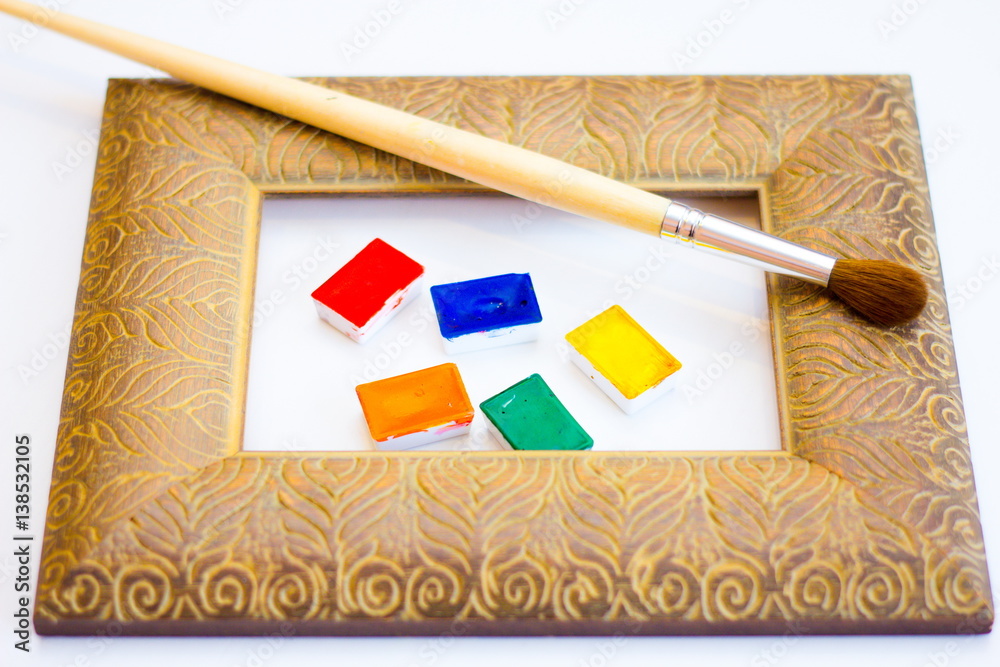 Obraz premium The palette of watercolor paints and brush and frame on a white background, closeup. Selective focus. Place for an inscription