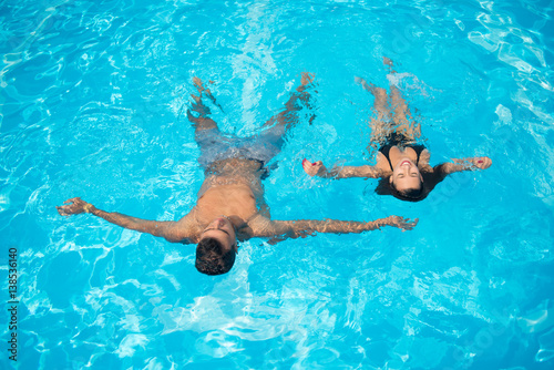 Couple floating on the surface in the swimming pool on the turquoise water at summer vacation