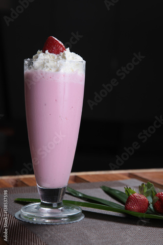 Strawberry Milkshake on Beautifully Decorated Restaurant Table with Dark Background. A delicious strawberry milkshake served in a tall glass, elegantly placed on a beautifully decorated restaurant