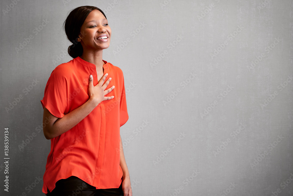 Black female business person busy laughing with one hand against her chest  while wearing a bright colourful orange blouse with space for copy text on  the right of the image. Stock Photo