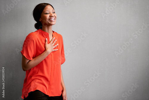 Black female business person busy laughing with one hand against her chest while wearing a bright colourful orange blouse with space for copy text on the right of the image. photo