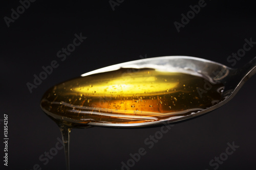 Honey pouring from spoon against a dark background