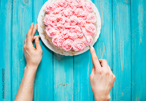 Woman's hands cut the cake with pink cream on blue wood background. Pink cake.