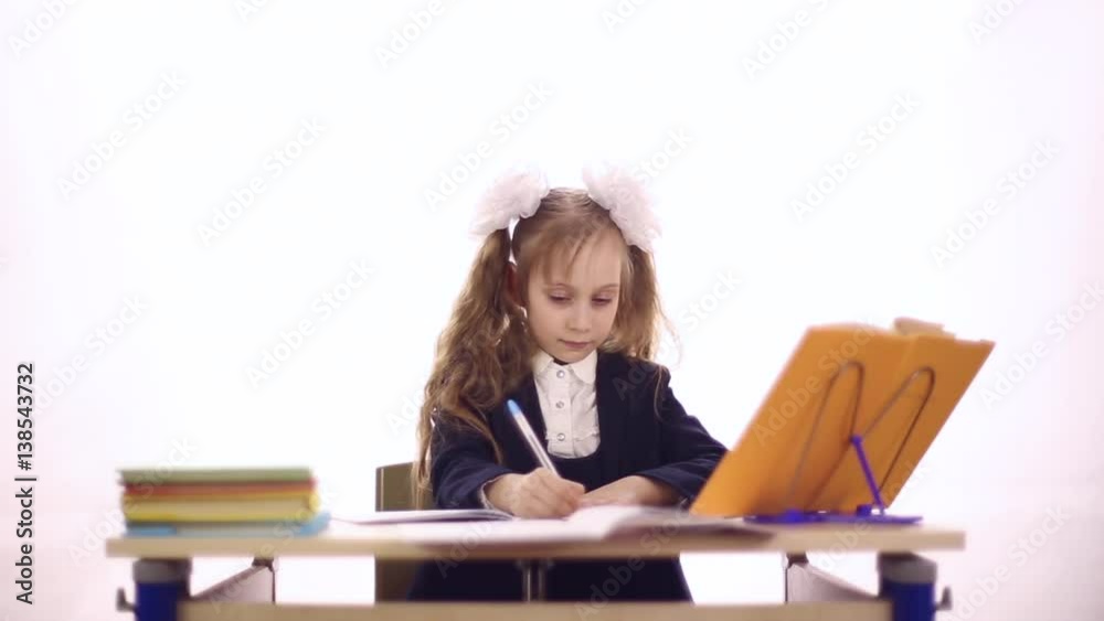 A girl dressed in a school uniform sitting at school desk, she writes in a notebook, textbooks on the table, she is showing thumb
A girl dressed in a school uniform sitting at school desk, she writes in a notebook, textbooks on the table, she is showing thumb