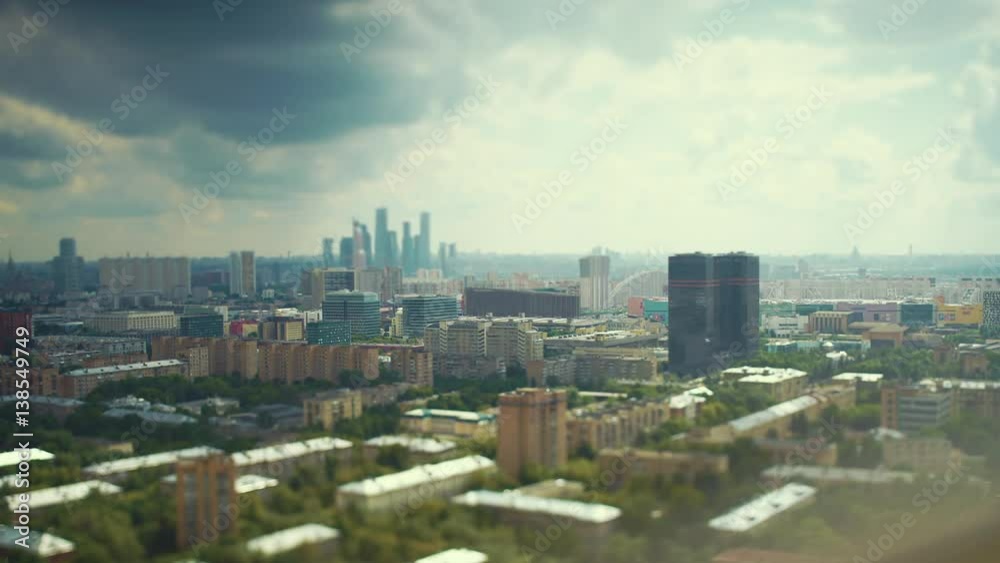 Tilt shift time lapse shooting of dark and cloudy sky above residential and business districts of big city with fast and strong moving shadows, clouds and rays of sunlight, skyscrapers on horizon Tilt shift time lapse shooting of dark and cloudy sky above residential and business districts of big city with fast and strong moving shadows, clouds and rays of sunlight, skyscrapers on horizon
