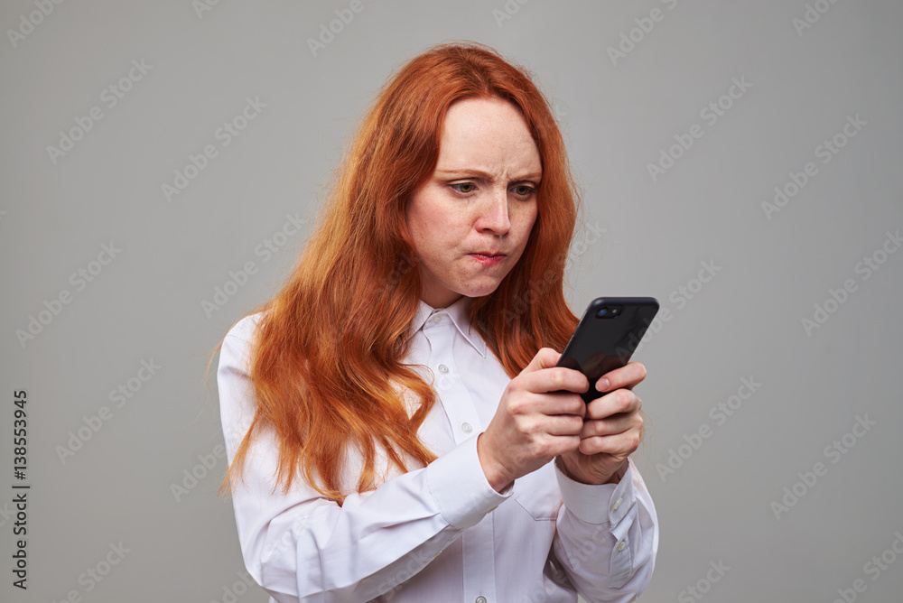 Hot-tempered girl with auburn hair pointing at the screen of telephone Hot-tempered girl with auburn hair pointing at the screen of telephone