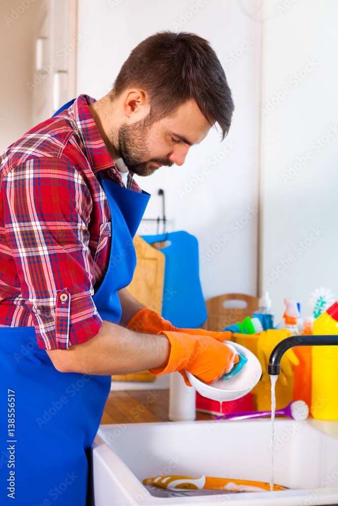Obraz premium Man makes cleaning the kitchen. Young man washes the dishes. Cleaning concept.
