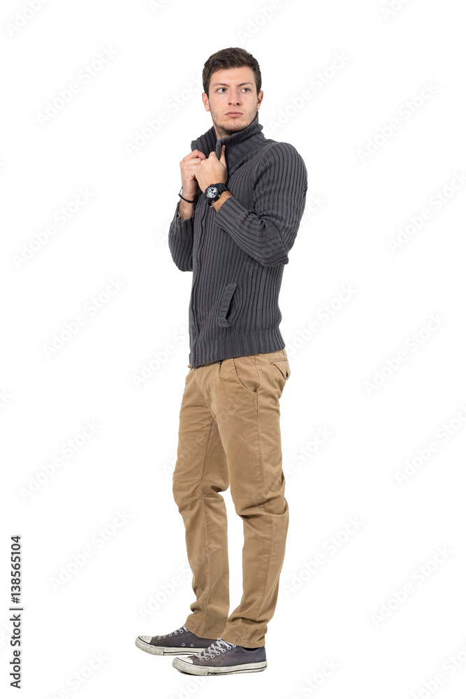 Side view of casual young man adjusting sweater collar look behind. Full body length portrait isolated over white background. Side view of casual young man adjusting sweater collar look behind. Full body length portrait isolated over white background.