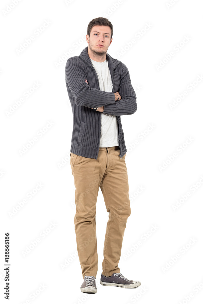 Serious young casual man in unzipped sweater with crossed arms looking at camera. Full body length portrait isolated over white background. Serious young casual man in unzipped sweater with crossed arms looking at camera. Full body length portrait isolated over white background.