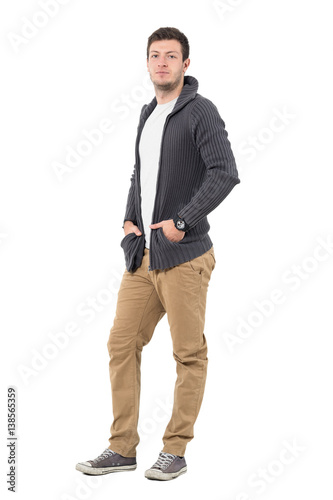 Handsome confident young man in ocher pants and gray sweater looking at camera. Full body length portrait isolated over white background.