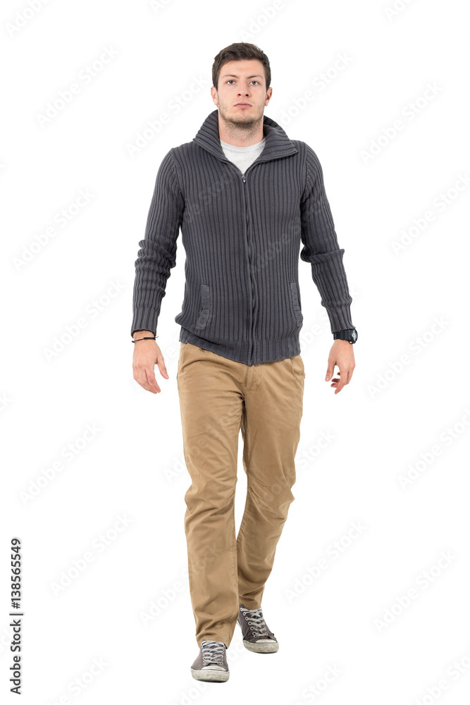 Serious unhappy man wearing zip jumper and beige pants walking at camera. Full body length portrait isolated over white background. Serious unhappy man wearing zip jumper and beige pants walking at camera. Full body length portrait isolated over white background.