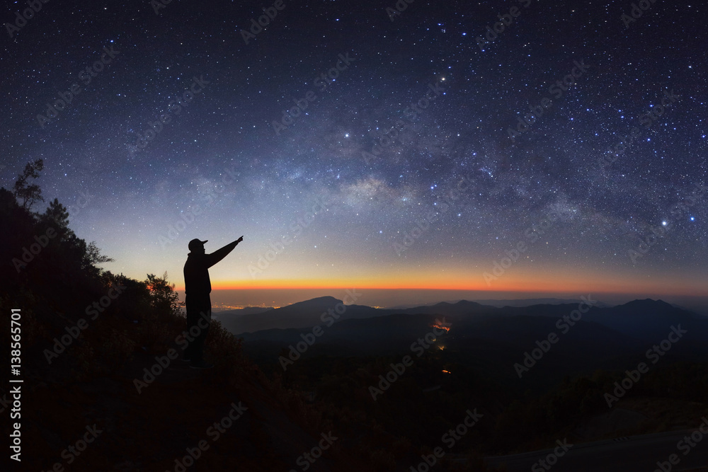 A Man is standing next to the milky way galaxy pointing on a bright star at Doi inthanon Chiang mai, Thailand.