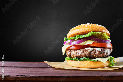 Craft beef burger on wooden table isolated on black background.