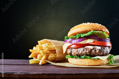 Craft beef burger and french fries on wooden table isolated on black background.
