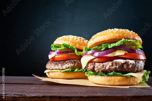 Two craft beef burgers on wooden table isolated on black background.