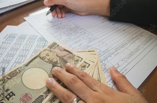 Woman hand hold pen fill in the details on the tax forms paper with yen moneyin business concept.