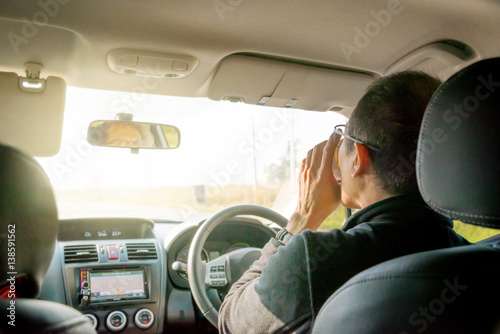 Asian middle aged man drinking coffee while driving his car.