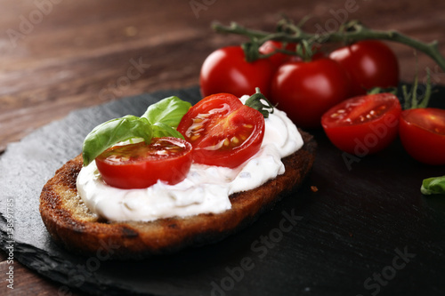 Bread with cream cheese and tomato for lunch table. Sharing antipasti on party or summer picnic time over wooden rustic background.