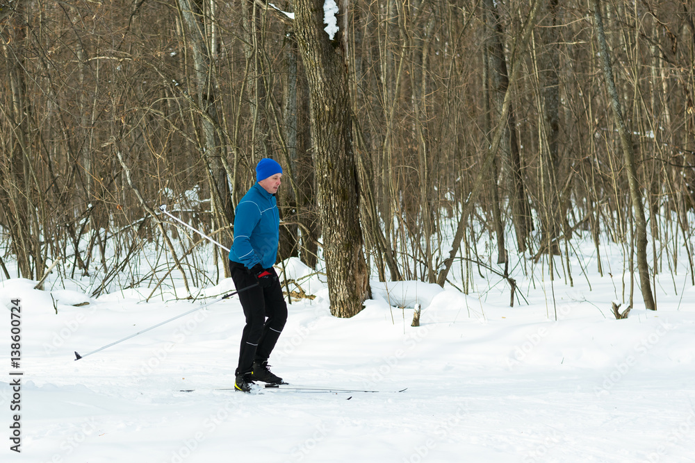 Man in a blue suit runs on skis in the winter woods.