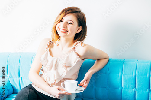 Portrait of attractive smiling womansitting in sofa with cup of coffee or tea in spa or beauty salon. photo