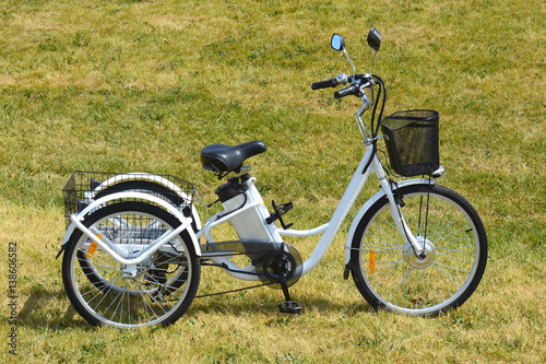 Electric trike or bicycle in the park in sunny summer day. Shot from the side. Unfiltered, with natural lighting. The view of the e motor and power battery of the three wheel bike.