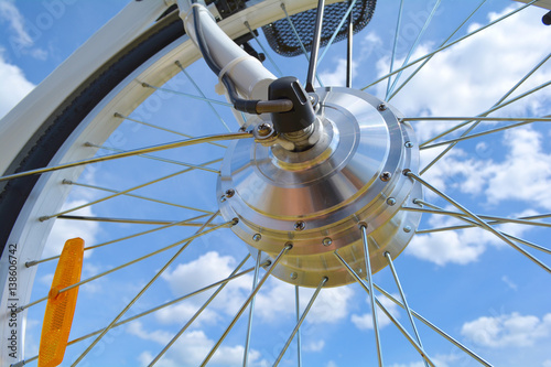 Wheel of the electric bicycle view from below. E bike motor with light reflections. Unfiltered, with natural lighting and blue sky and clouds.