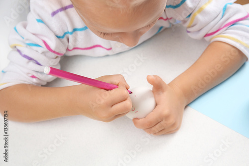 Cute little girl painting egg for Easter while sitting at table  closeup