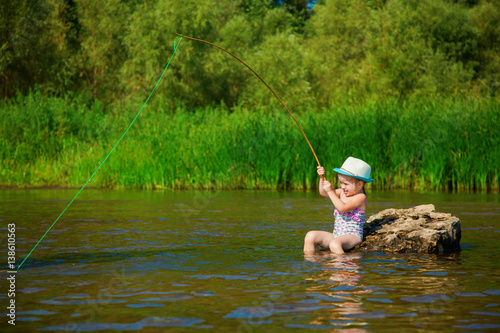 Little girl with toy fishing tackle plays on river stone