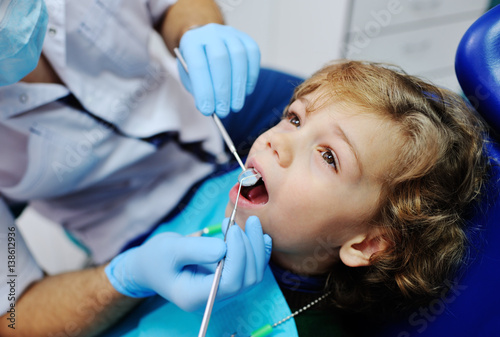 Male dentist examines the teeth of the patient cheerful child with curly red hair. Moloi boy smiling in dentist's chair. child mouth wide open in the dentist's chair
