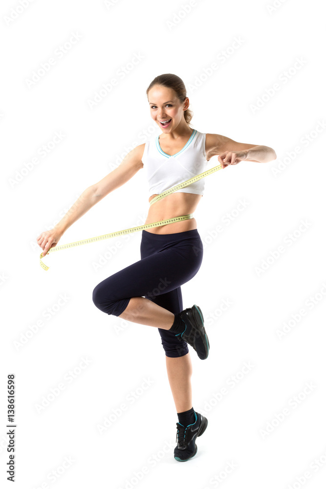Smiling woman in sportswear measuring her waist measure tape.