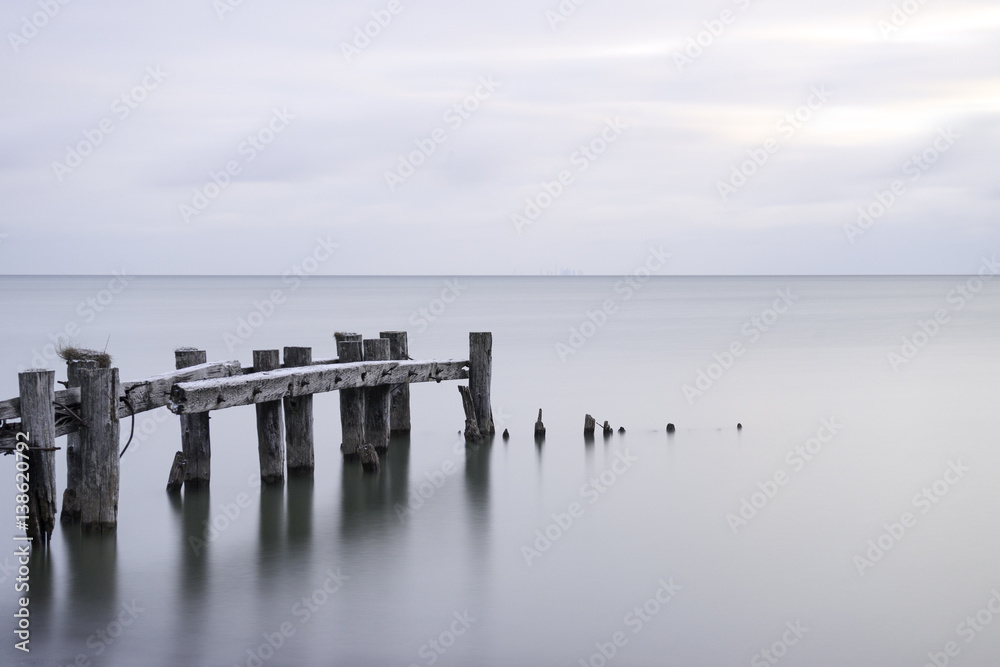 Posts of a broken pier leading out into calm blue tranquil sea water