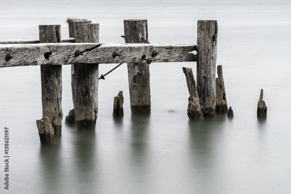 End of an old broken pier, closeup of posts standing in calm tranquil water