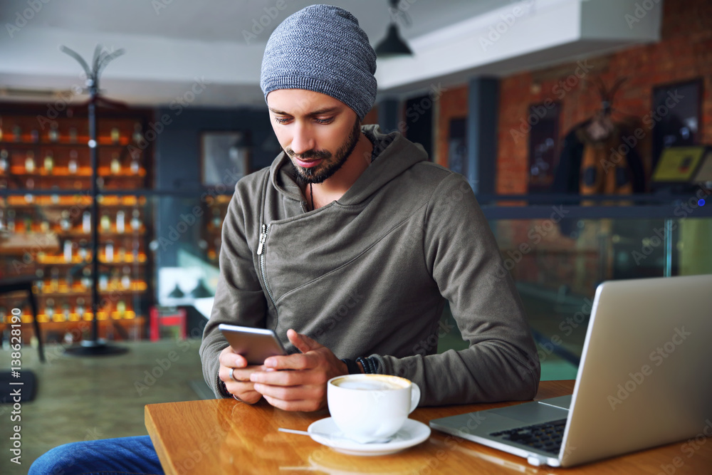 Young handsome hipster guy at the restaurant using a mobile phone. Young handsome hipster guy at the restaurant using a mobile phone.