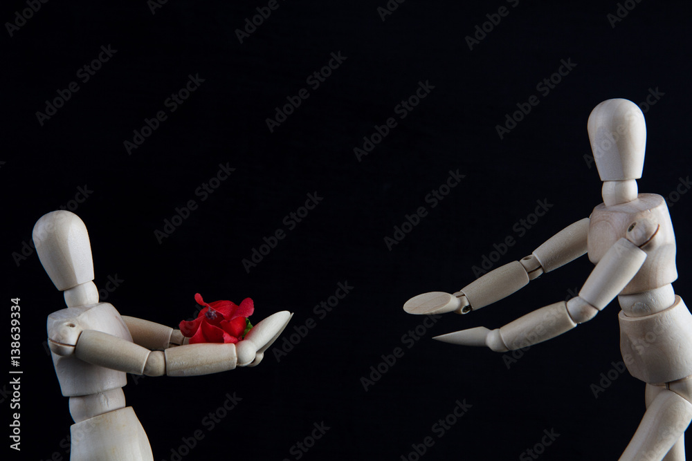Wooden figurines offering flower on black background with copy space. Wedding, engagement, valentines day concept Wooden figurines offering flower on black background with copy space. Wedding, engagement, valentines day concept